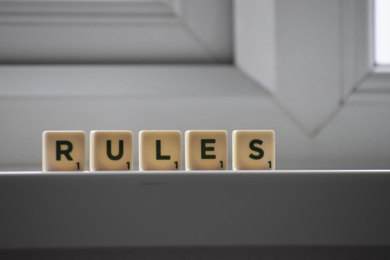 Het woord 'Rules' gespeld met Scrabble-achtige stenen op een lichte achtergrond.