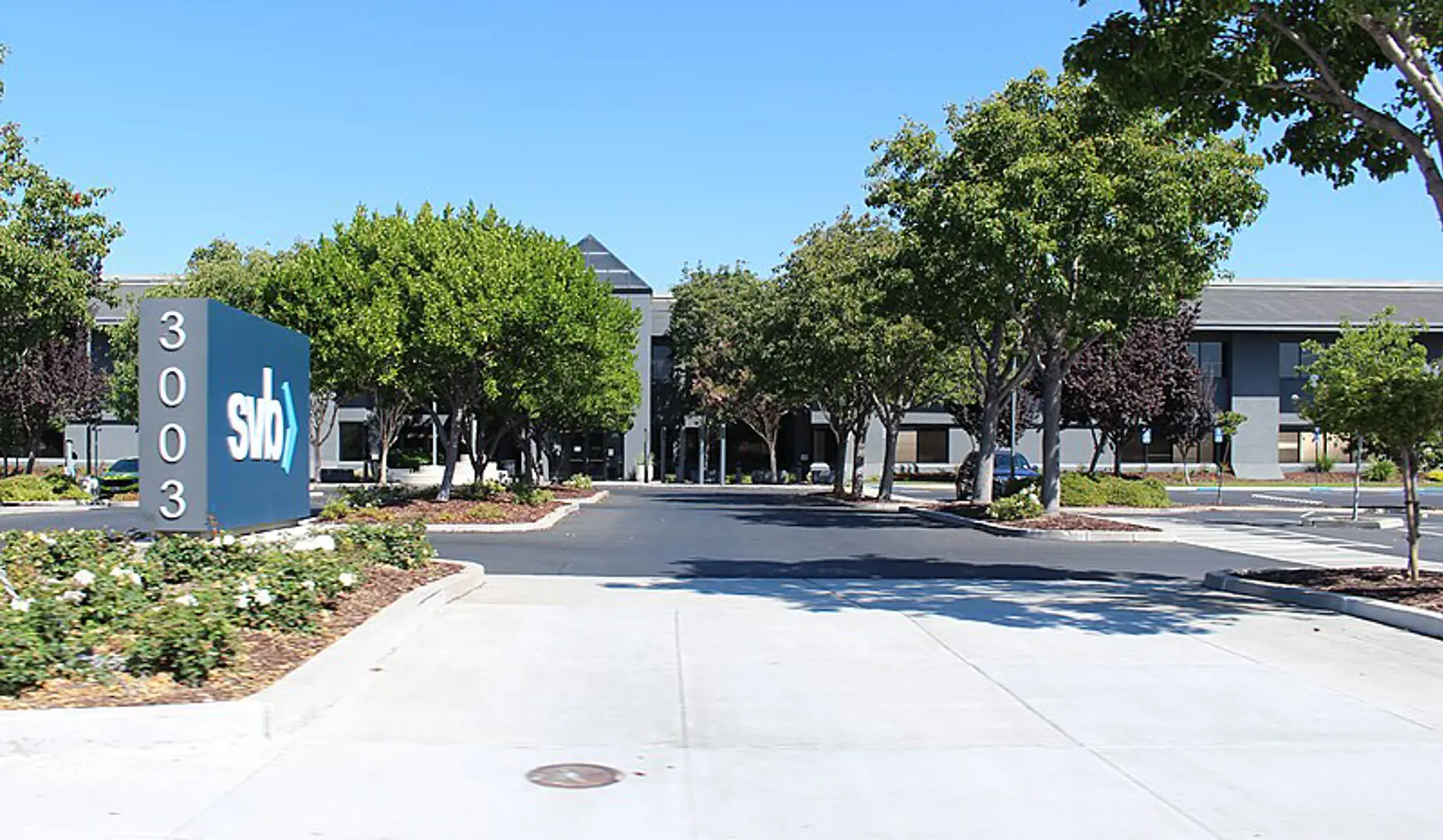 Het kantoor van Silicon Valley Bank aan Tasman Drive in San Jose, Californië, met moderne glazen gevels en groene bomen langs de weg.