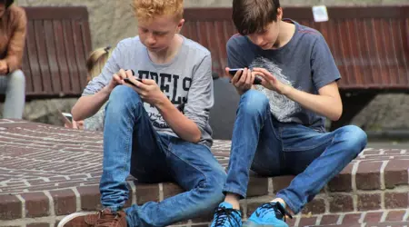 Twee kinderen die op straat zitten met aandacht op hun telefoons.