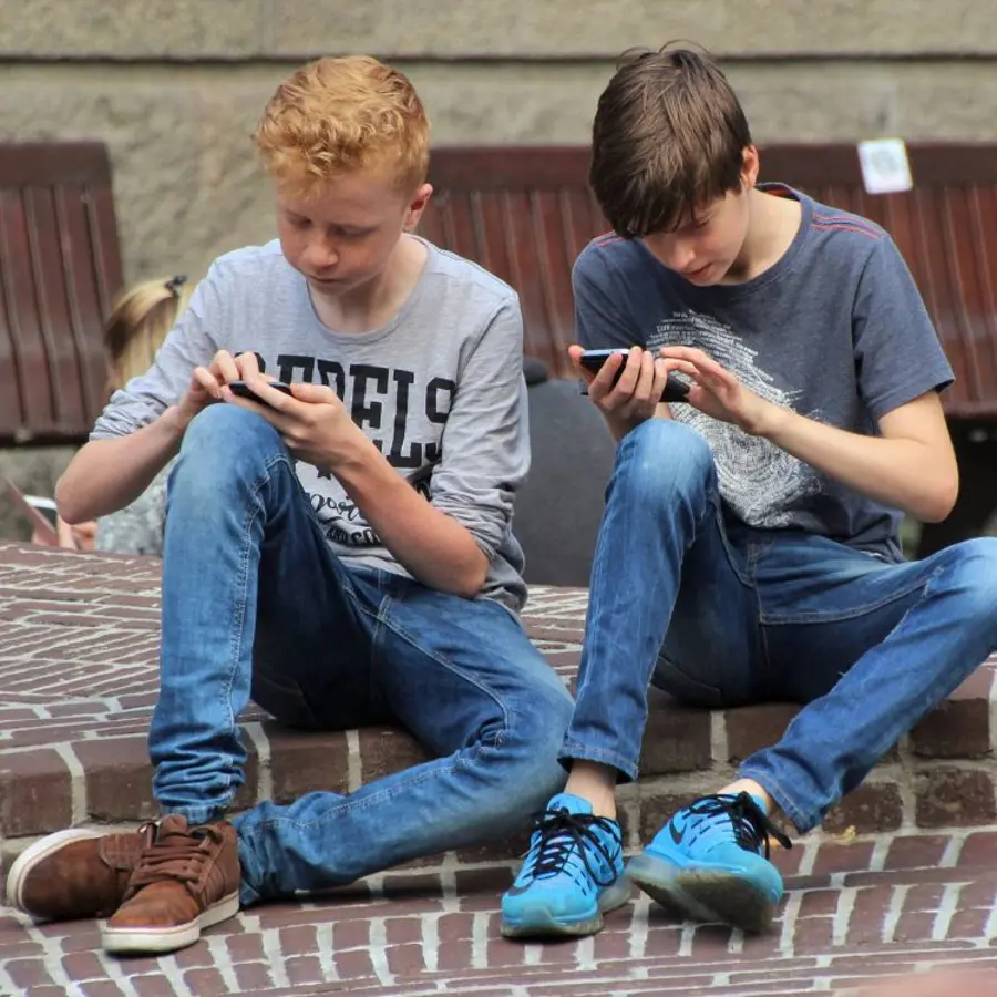 Twee kinderen die op straat zitten met aandacht op hun telefoons.