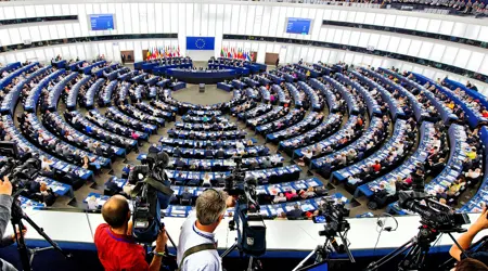 Vergadering in het Europees Parlement met volle zaal en cameramensen op de voorgrond.